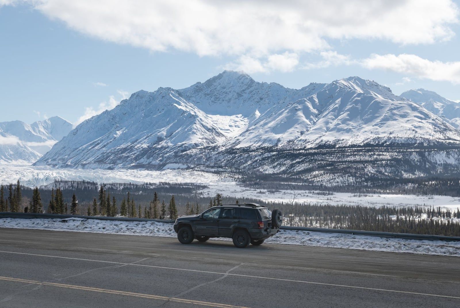 An SUV parked along the snowy Glenn Highway overlooking Matanuska Glacier and the Chugach Mountains.